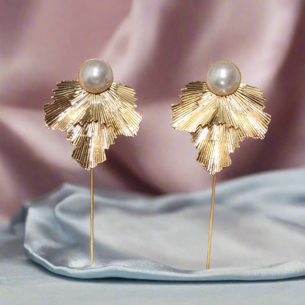 Pair of gold earrings with pearl centers on a gray background