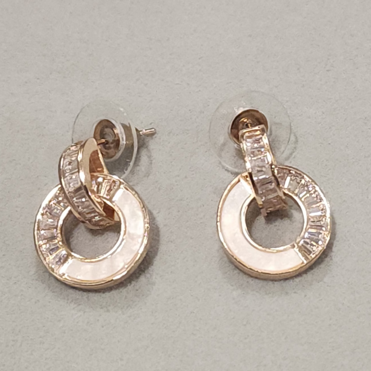 Pair of gold stud earrings with clear stones on a light gray background
