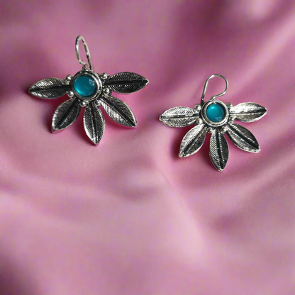 Silver leaf-shaped earrings with turquoise stones on a light gray background