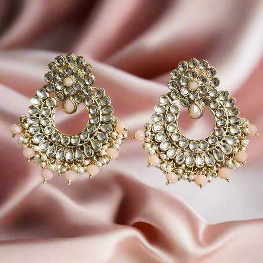 Pair of ornate earrings with gold and pink stones on a gray surface